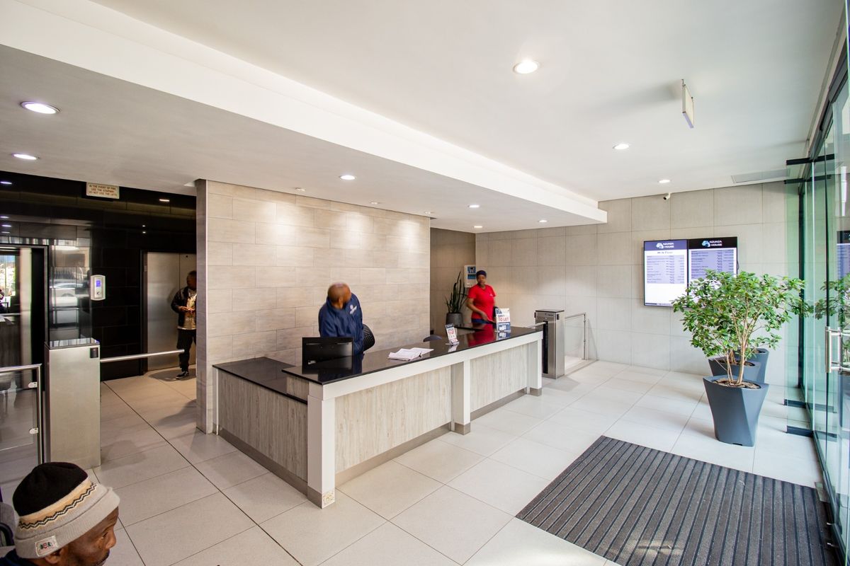 Modern commercial building lobby featuring a professional reception desk, tiled flooring, elevator access, and integrated digital signage for tenant information.