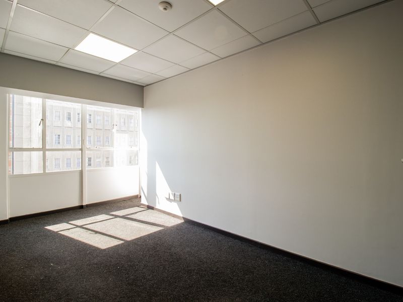 A bright, empty office space featuring a suspended ceiling, recessed lighting, and large windows providing natural light.