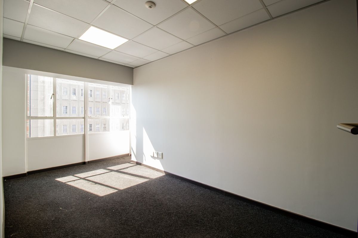 A bright, empty office space featuring a suspended ceiling, recessed lighting, and large windows providing natural light.