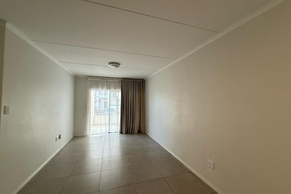 An empty, neutral-toned living room featuring tiled flooring and a sliding glass door providing access to an outdoor area.