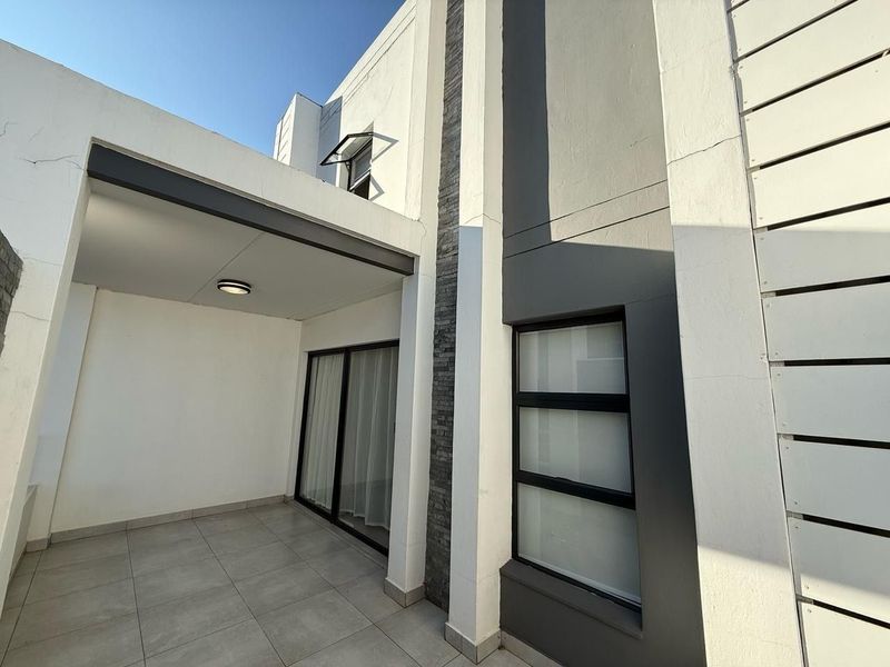 A modern covered patio area featuring tiled flooring, a stone-clad feature wall, and sliding glass door access to the interior.