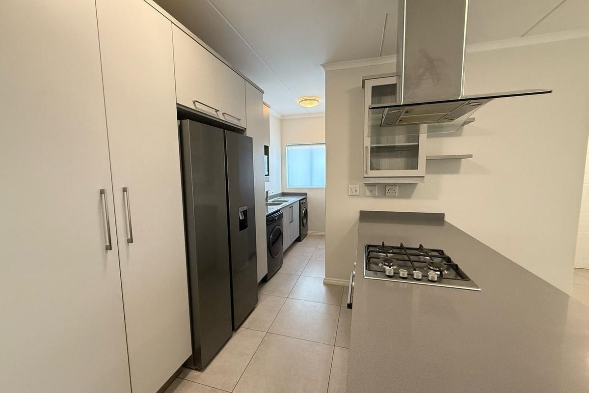 Modern kitchen featuring sleek white cabinetry, stone countertops, a gas hob with extractor fan, and dedicated space for appliances.