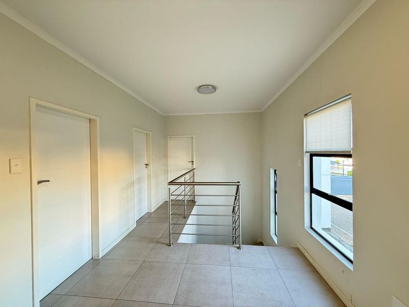 A bright and spacious upper-level landing featuring tiled flooring, a modern stainless steel balustrade, and neutral wall finishes.
