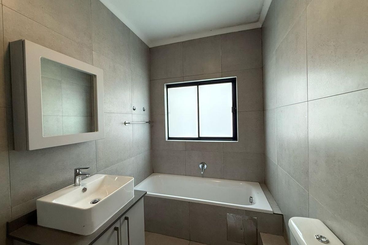 A modern, neutral-toned bathroom featuring a built-in vanity with a ceramic basin, a bathtub, and a toilet, finished with floor-to-ceiling wall tiles.