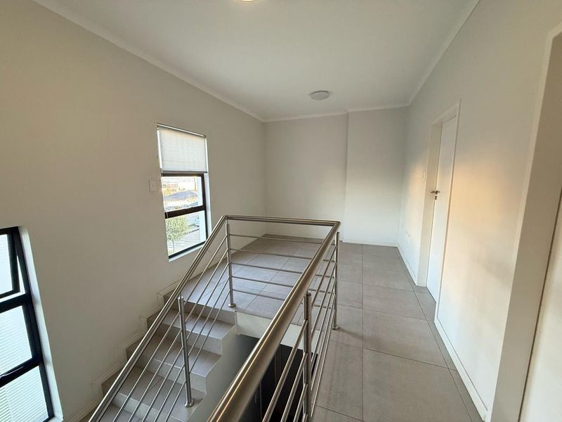 A bright, modern landing area featuring tiled flooring and a sleek stainless steel balustrade overlooking the staircase.