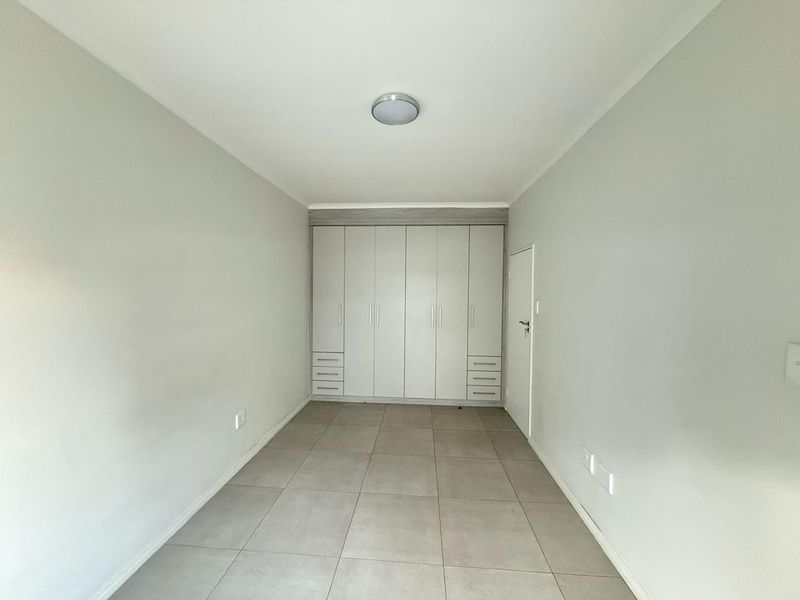 A clean, empty bedroom featuring neutral tiled flooring and extensive built-in cabinetry with a modern finish.
