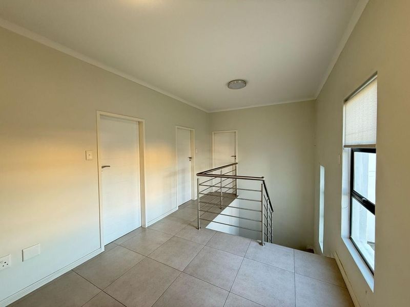 A bright and spacious landing area featuring tiled flooring, a modern stainless steel balustrade, and access to multiple rooms.