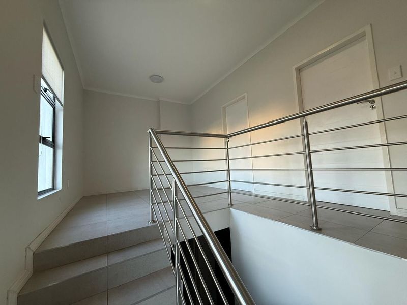A bright, modern landing area featuring tiled flooring and a sleek stainless steel balustrade overlooking the staircase.