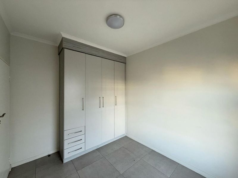 A clean, empty bedroom featuring neutral wall tones, modern grey floor tiles, and a functional built-in wardrobe with integrated drawers.