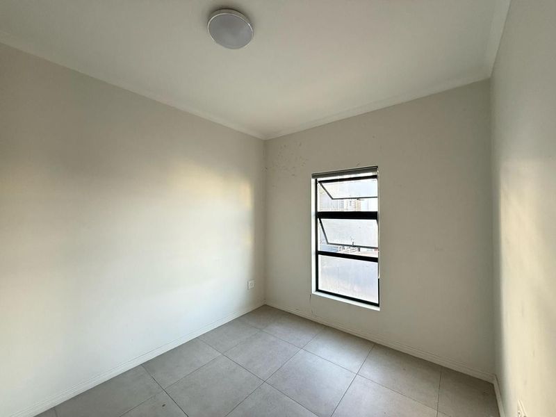 A vacant bedroom featuring neutral tiled flooring, a single aluminium window, and a ceiling-mounted light fixture.