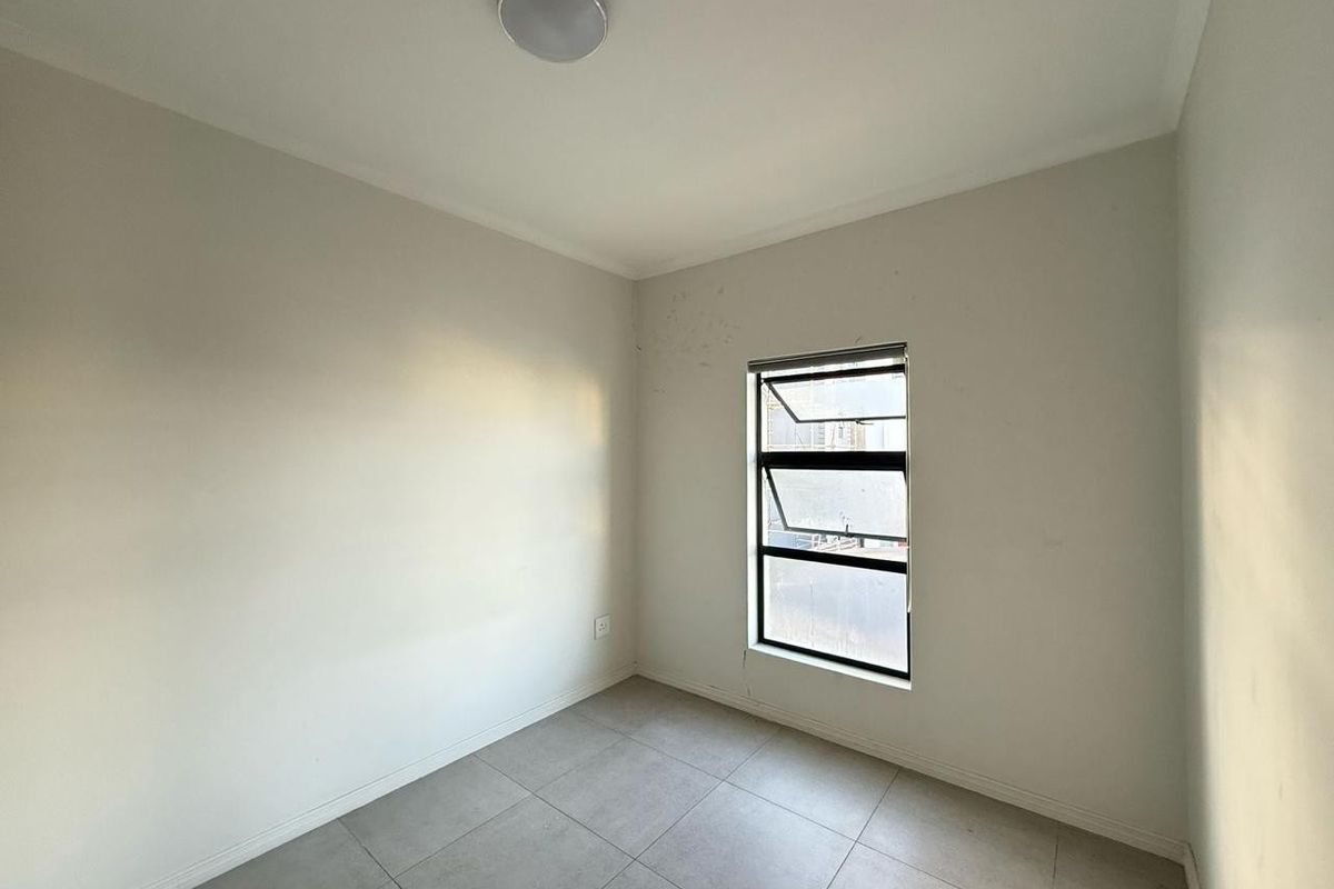 A vacant bedroom featuring neutral tiled flooring, a single aluminium window, and a ceiling-mounted light fixture.