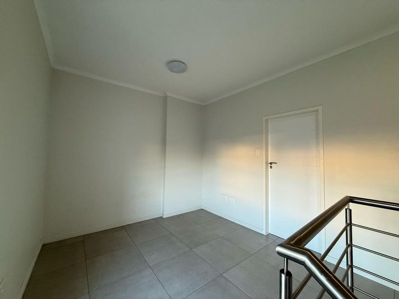 A clean, empty landing area featuring neutral tiled flooring and a modern stainless steel balustrade, providing a bright and versatile transition space.