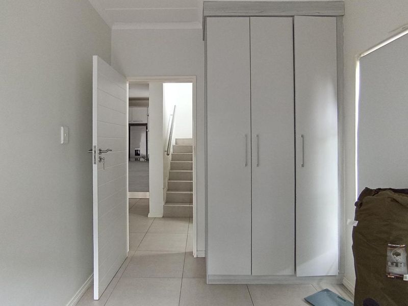 A bright, neutral hallway featuring tiled flooring and built-in storage cupboards, providing access to the staircase and adjacent living areas.