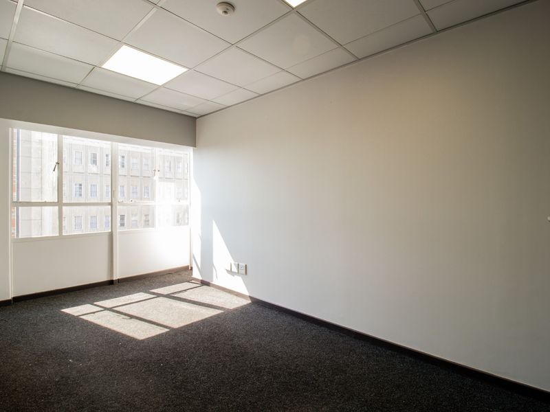 A bright, empty office space featuring a suspended ceiling, recessed lighting, and carpeted flooring, offering a clean and professional environment.