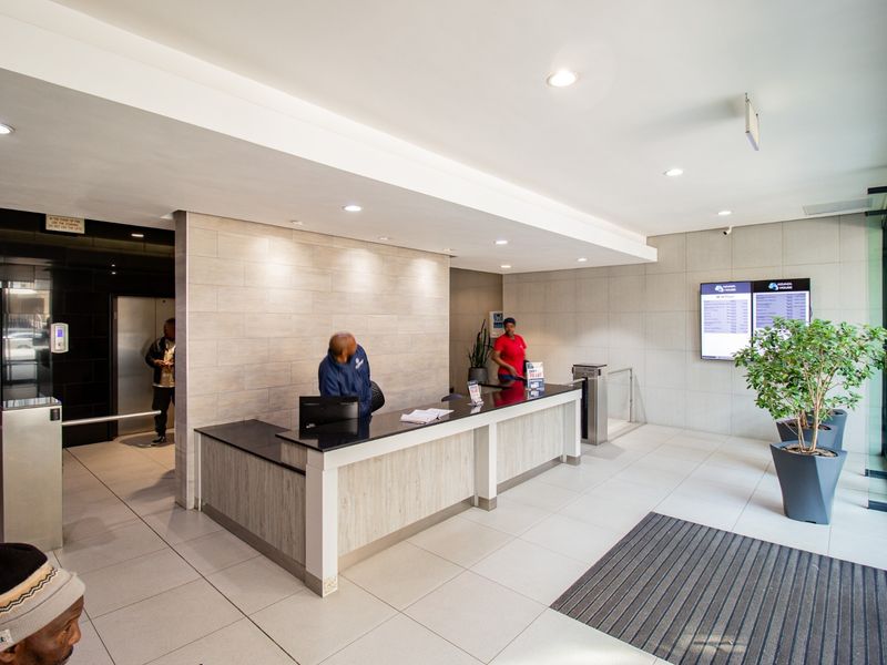 Modern commercial building lobby featuring a reception desk, security turnstiles, elevator access, and professional tiled finishes.