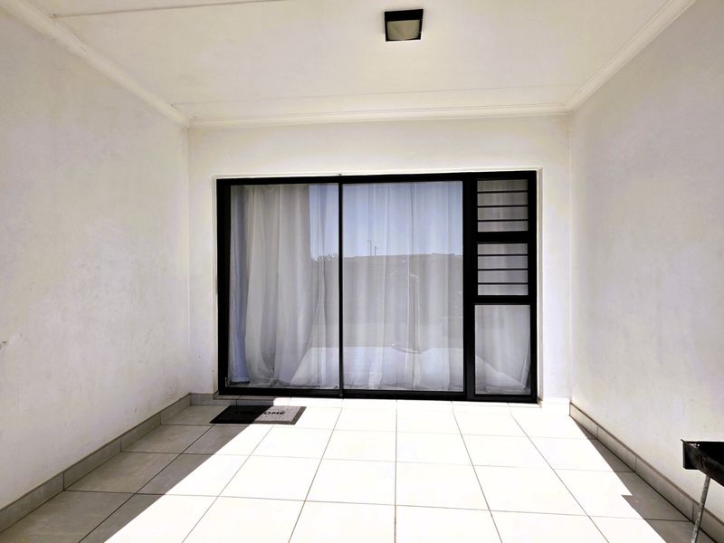 A clean, covered patio area featuring white tiled flooring and a large sliding glass door with integrated louvre window.