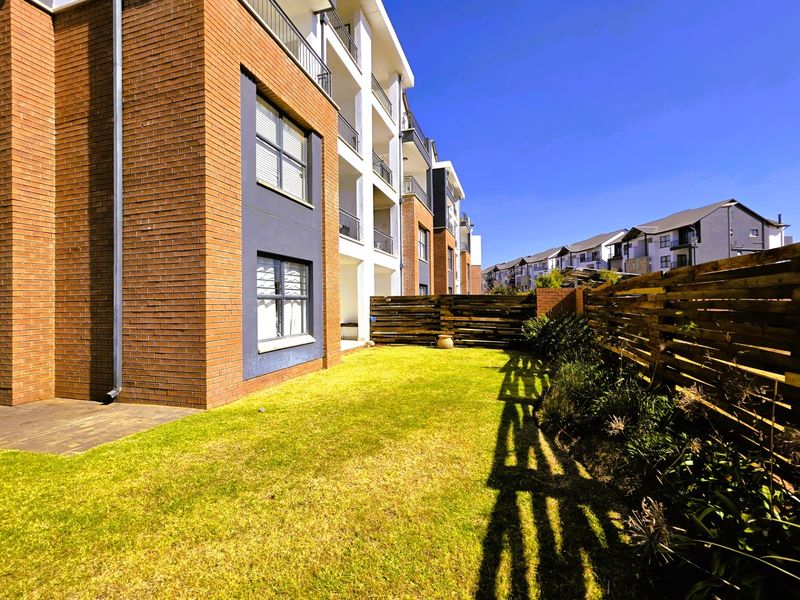 A view of the rear exterior of the apartment building, featuring a private garden, timber fencing, and paved patio area.