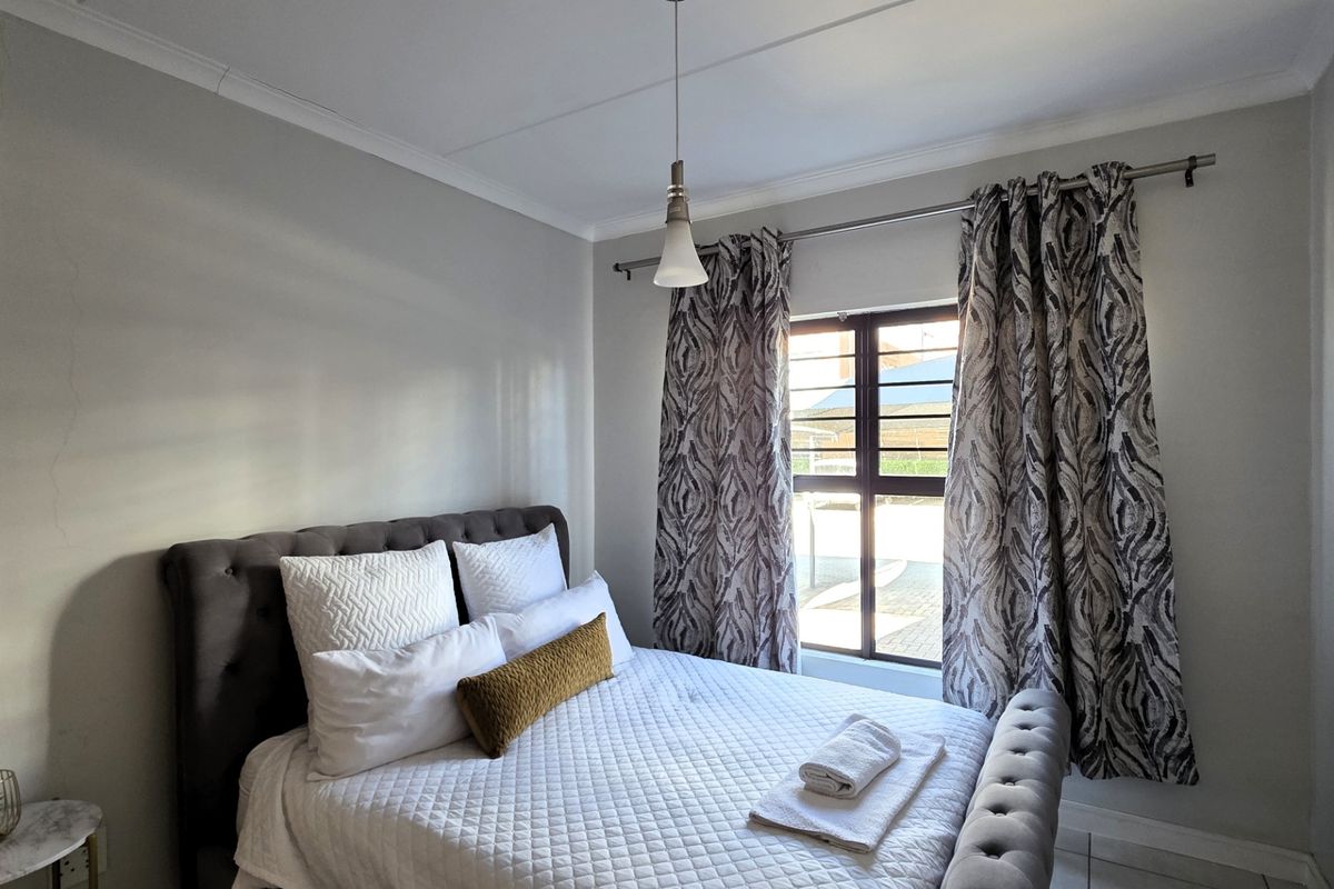 A well-lit bedroom featuring tiled flooring, decorative cornicing, and a window fitted with security bars.