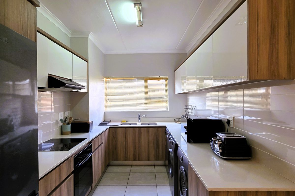 Modern galley-style kitchen featuring wood-grain cabinetry, stone countertops, integrated appliances, and a tiled backsplash with ample storage space.
