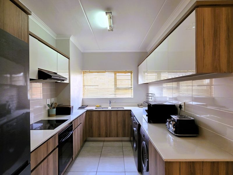 Modern galley-style kitchen featuring wood-grain cabinetry, stone countertops, integrated appliances, and a tiled backsplash with ample storage space.