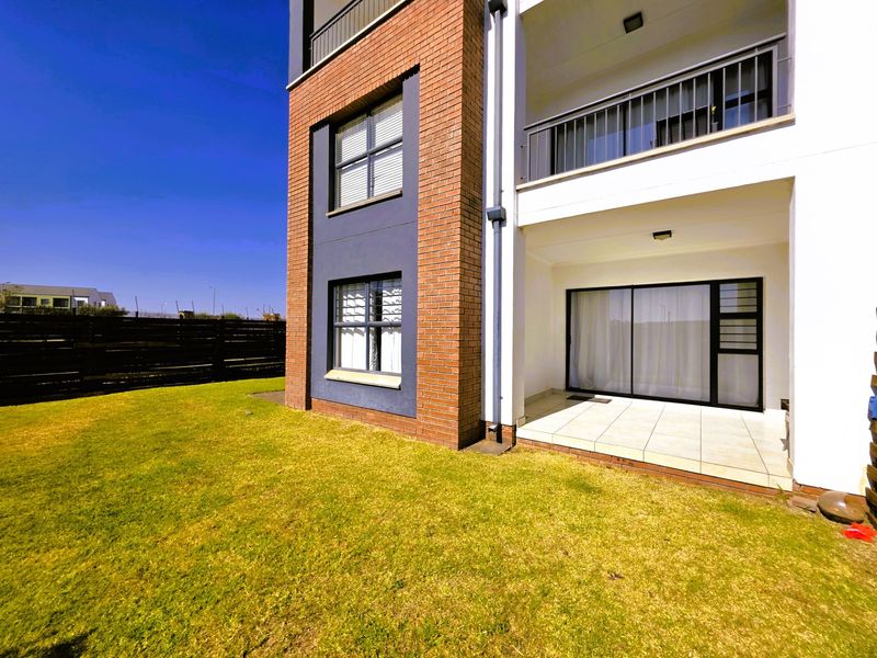 Rear view of a modern apartment building featuring a brick facade, a ground-floor tiled patio with sliding doors, and an upper-level balcony.