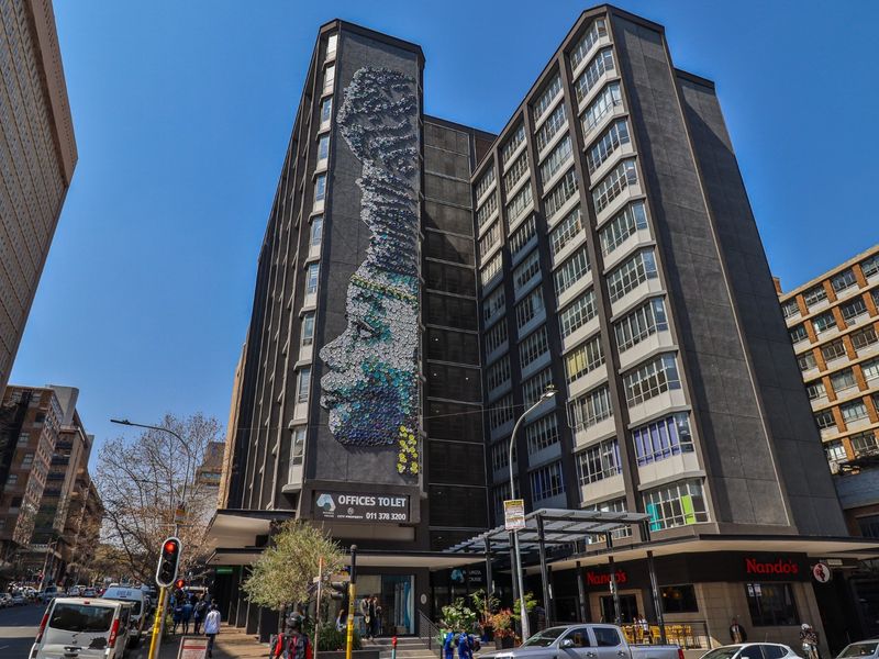 A prominent multi-story commercial building featuring a striking large-scale mural on the facade, with ground-level retail space and street-level access.