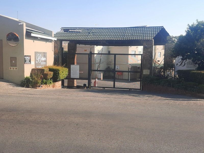 The main entrance to the apartment complex featuring a secure gated access point, brick pillars, and a tiled roof structure.