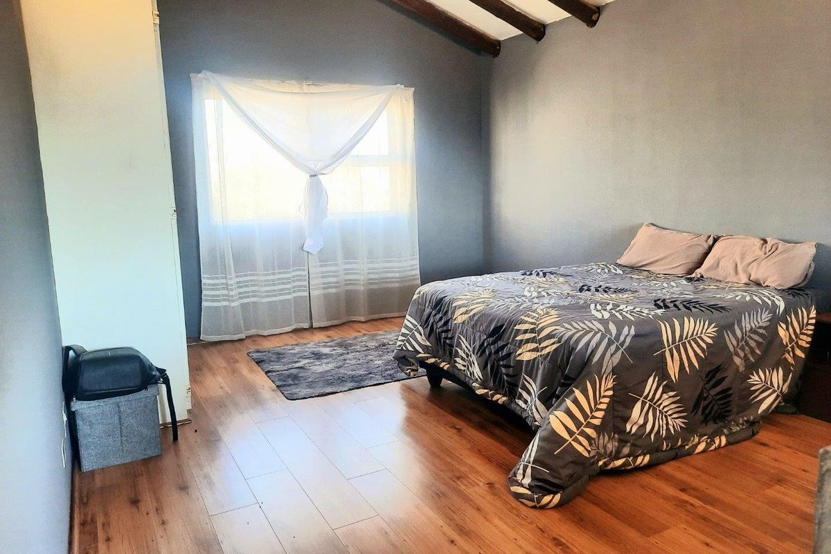 A bedroom featuring laminate flooring, exposed timber ceiling beams, and a built-in wardrobe, offering a cozy atmosphere with natural light.