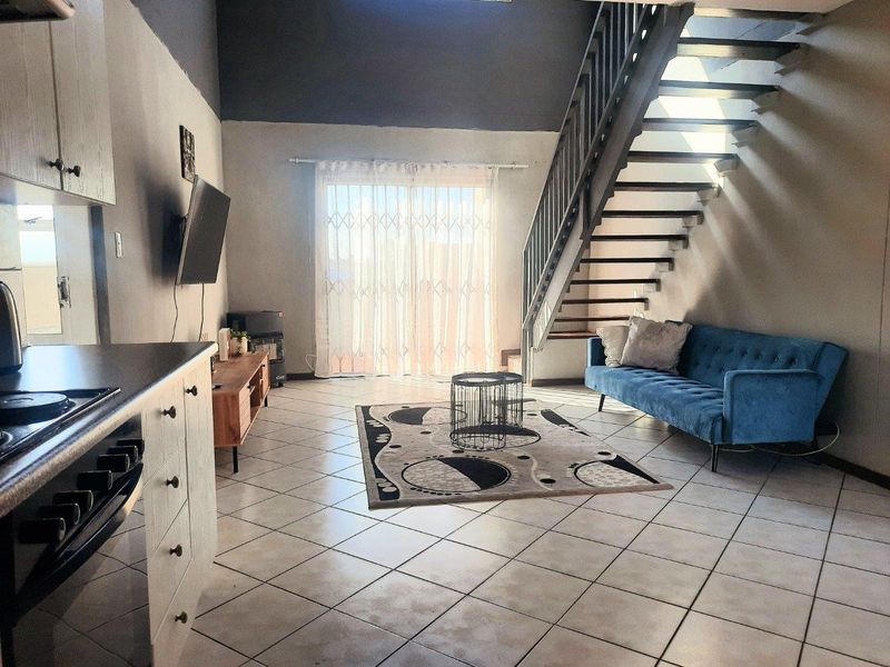 Open-plan living area featuring a kitchen with built-in appliances, tiled flooring, and a staircase leading to the upper level with access to a balcony.