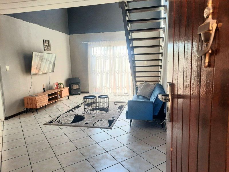 Open-plan living area featuring tiled flooring, a staircase leading to the upper level, and a sliding glass door with security gate access.