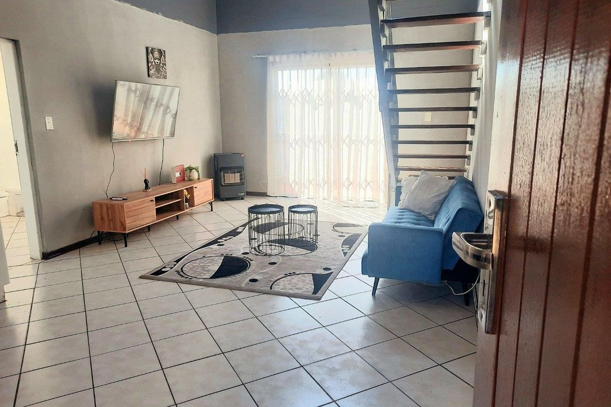 A living room featuring tiled flooring, a staircase, and a sliding glass door with a security gate leading to the exterior.