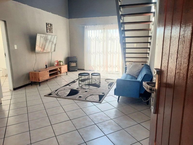 A living room featuring tiled flooring, a staircase, and a sliding glass door with a security gate leading to the exterior.