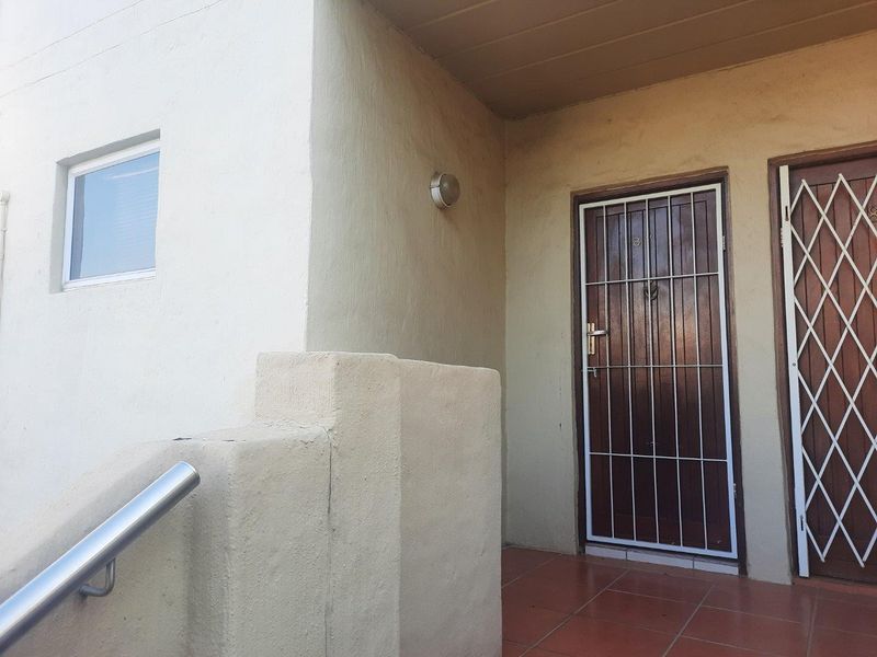 Entrance area featuring a secure timber door with a metal security gate, tiled flooring, and a stainless steel handrail.