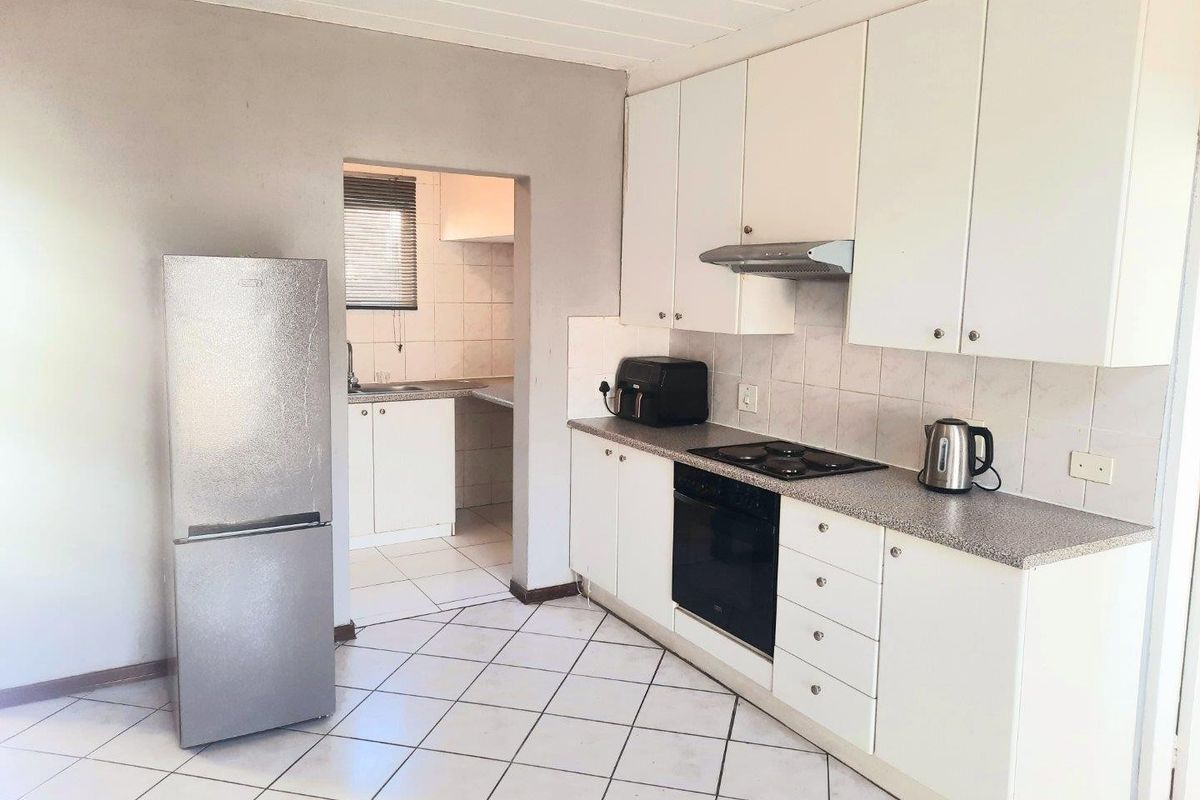 Functional kitchen featuring white cabinetry, granite-look laminate countertops, built-in oven, hob, and extractor fan, with an adjoining scullery area.