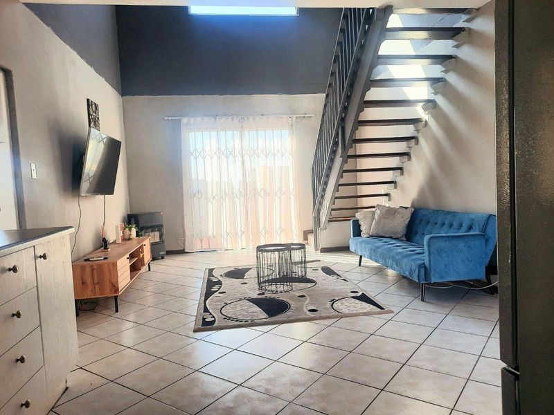 Open-plan living area featuring tiled flooring, a modern staircase, and a sliding glass door leading to an outdoor space with natural light.