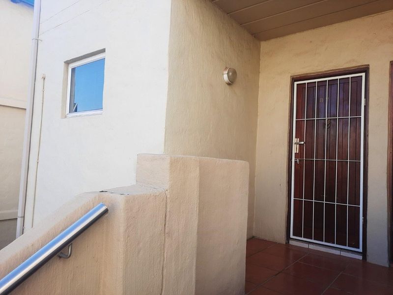 Entrance area featuring a secure metal gate, tiled porch flooring, and a stainless steel handrail leading to the front door.