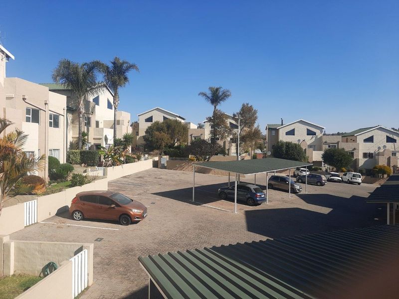 An elevated view of the apartment complex parking area featuring paved surfaces, covered carports, and surrounding residential building facades.