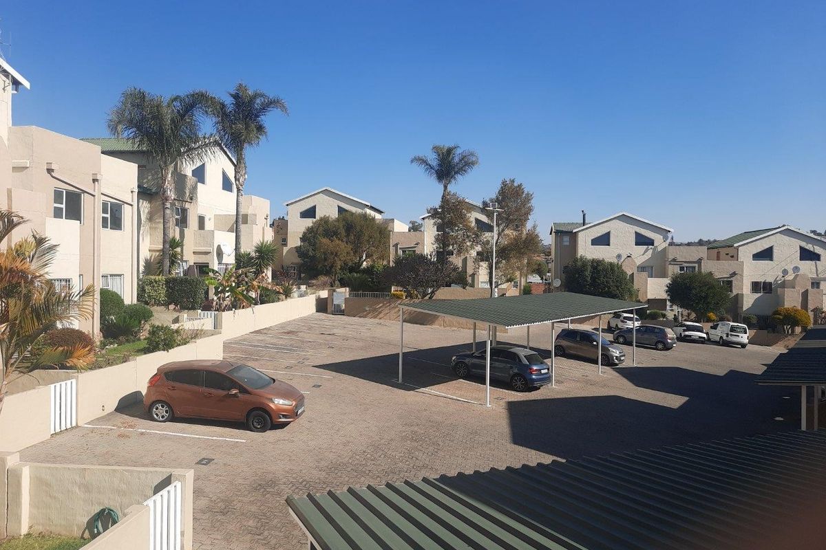An elevated view of the apartment complex parking area featuring paved surfaces, covered carports, and surrounding residential building facades.