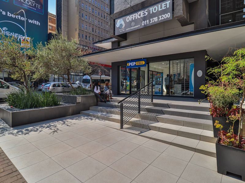 Modern commercial storefront entrance featuring tiled steps, metal handrails, and integrated planters, providing clear street-level access to the office building.