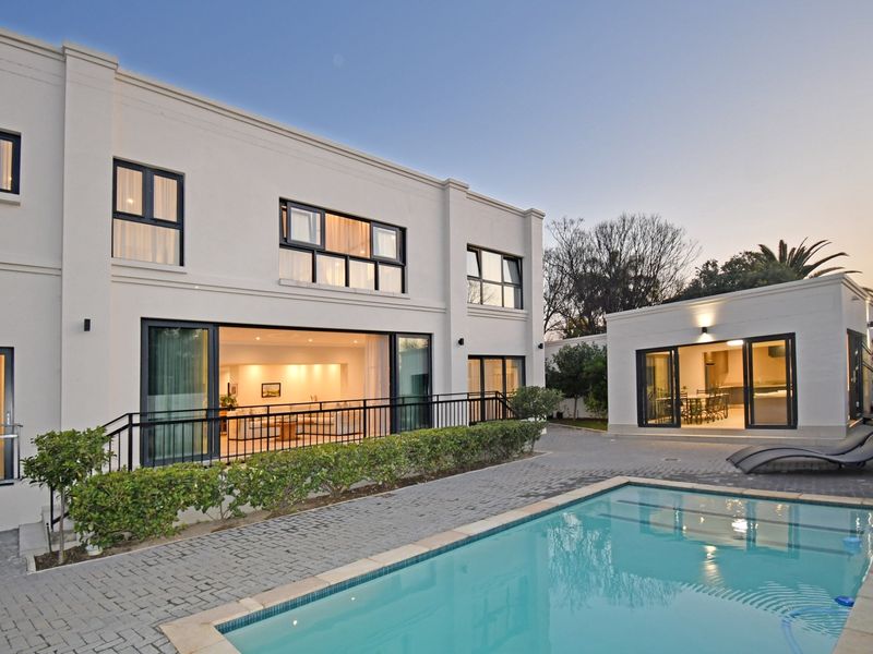 A modern rear exterior view featuring a swimming pool, paved patio area, and large sliding glass doors connecting to the main residence and outbuilding.
