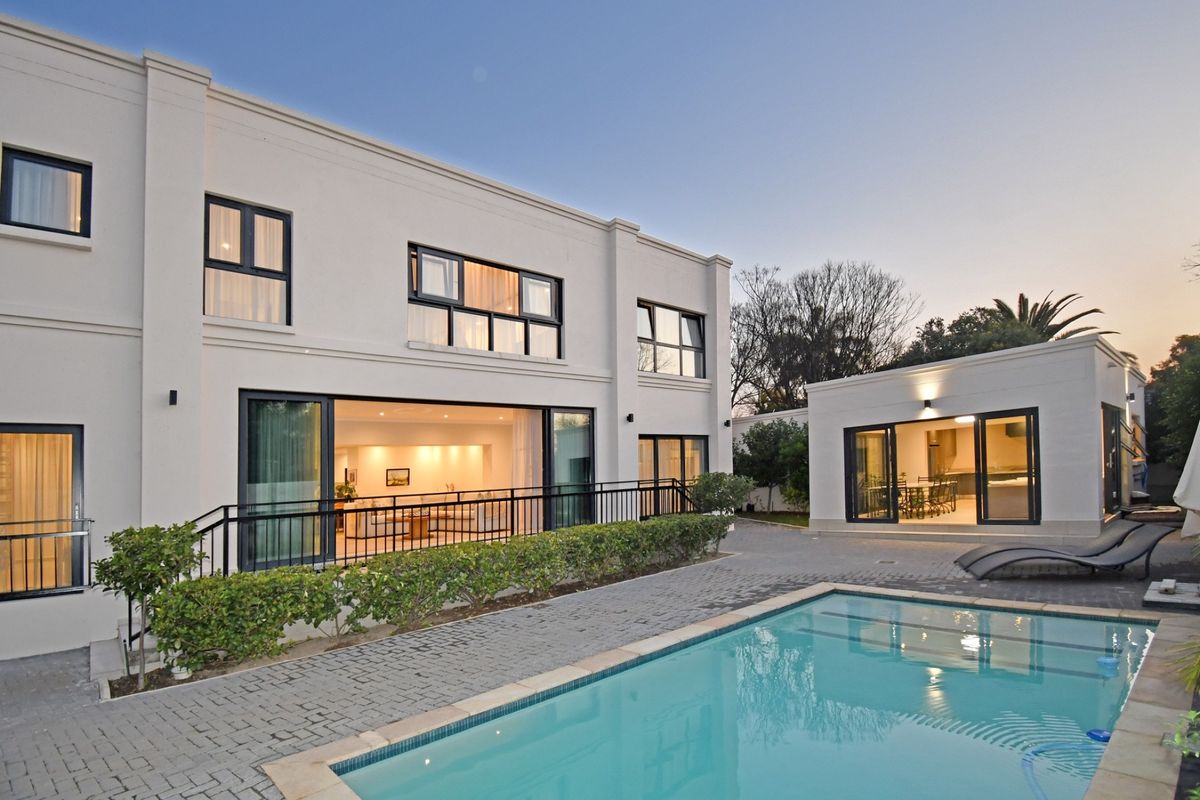 A modern rear exterior view featuring a swimming pool, paved patio area, and large sliding glass doors connecting to the main residence and outbuilding.