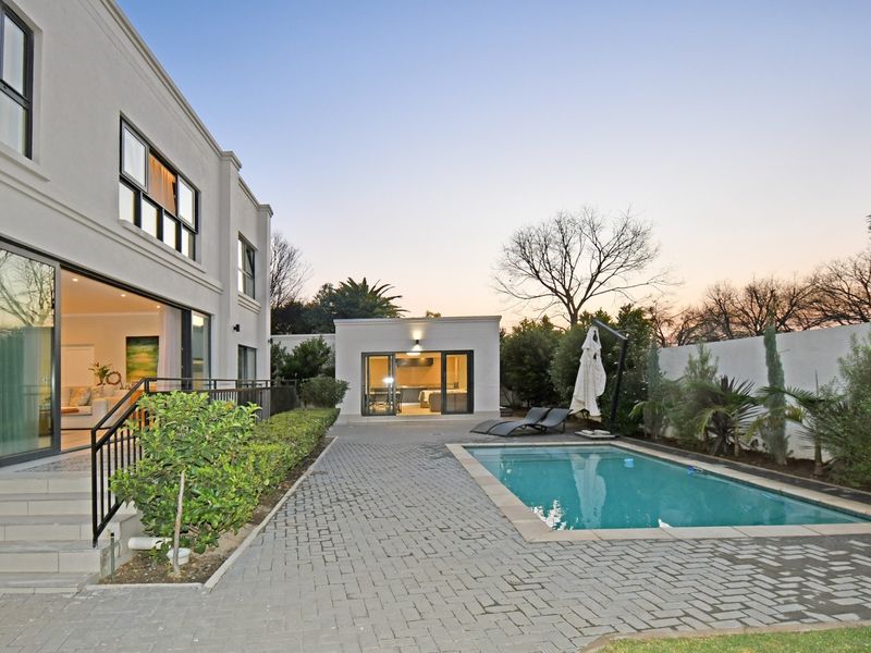 A well-maintained rear exterior featuring a paved patio, swimming pool, and direct access to the main house and a separate outbuilding.