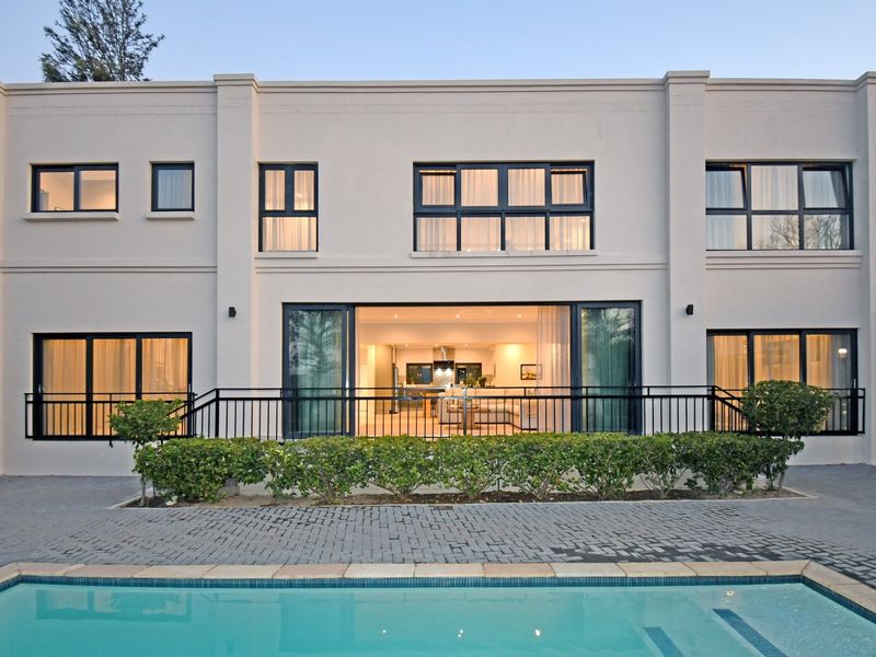 Rear elevation of a modern two-story home featuring a swimming pool, paved patio area, and large sliding glass doors opening into the living space.