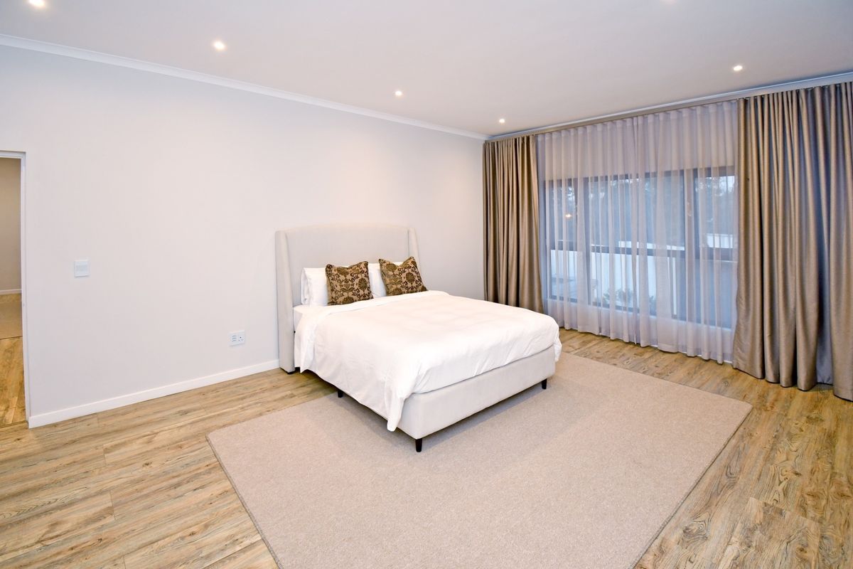 A bright and spacious bedroom featuring modern laminate flooring, recessed downlighting, and large sliding glass doors with floor-to-ceiling curtains.