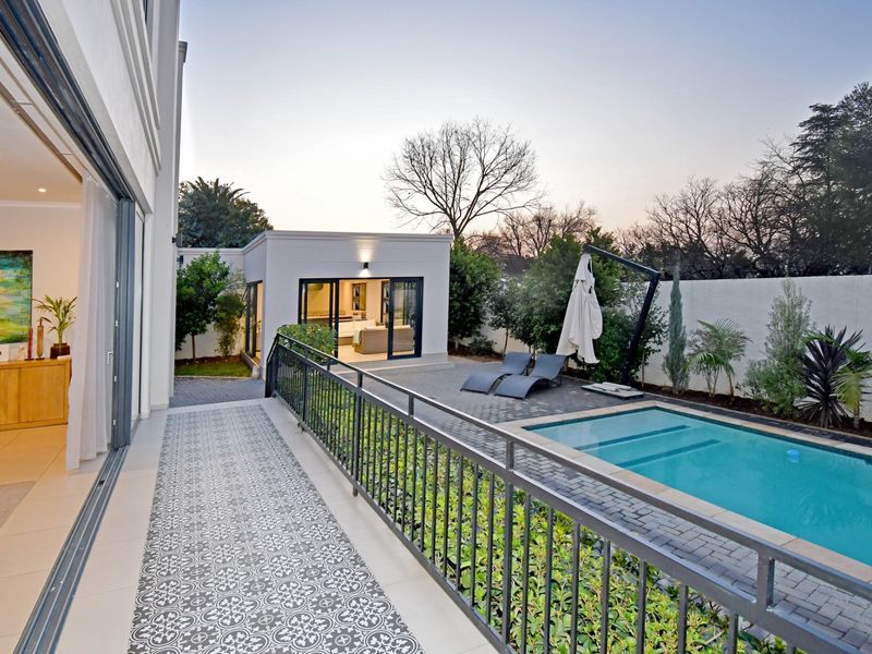 A well-maintained outdoor entertainment area featuring a swimming pool, paved patio, and a modern metal balustrade, seamlessly connected to the main residence.