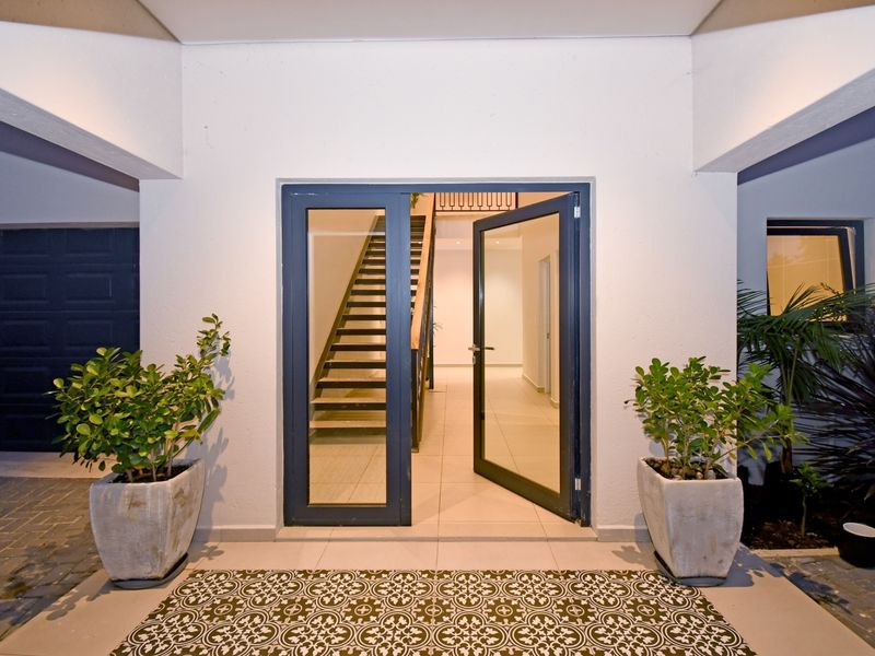 A modern, well-maintained entrance featuring a glass-panelled door, tiled porch area, and a clear view into the interior staircase.