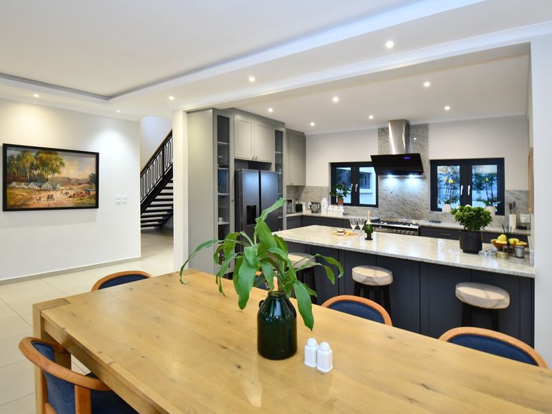 Modern open-plan kitchen and dining area featuring a large stone-topped island, contemporary cabinetry, and integrated appliances, seamlessly connected to the home's staircase.
