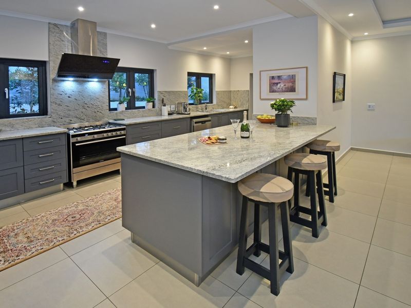 Modern kitchen featuring a large central island with granite countertops, high-end gas stove, extractor fan, and ample built-in cabinetry with recessed lighting.