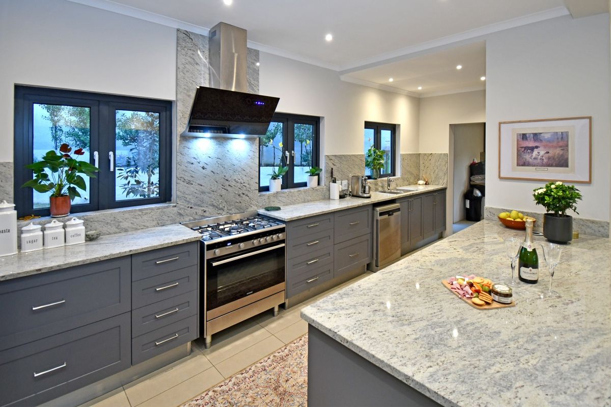 Modern kitchen featuring high-quality granite countertops, shaker-style cabinetry, a gas stove with extractor fan, and a spacious central island.