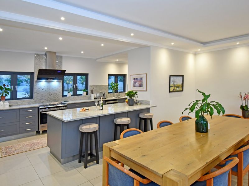 Modern open-plan kitchen and dining area featuring a central island with stone countertops, high-end cabinetry, and recessed lighting throughout.